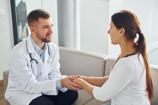 Holding patient by hands. Professional medic in white coat is in the clinic.