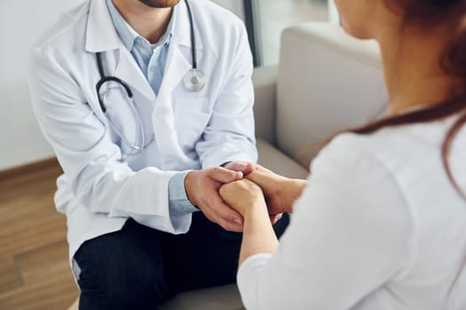 Holding patient by hands. Professional medic in white coat is in the clinic.