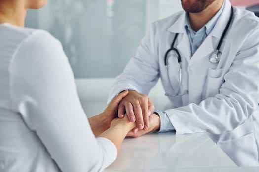 Holding patient by hands. Professional medic in white coat is in the clinic.