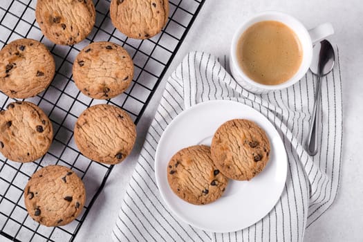 Close-up of baked oatmeal cookies with chocolate chips on a metal cooling rack and coffee in a white porcelain mug. Selective focus.