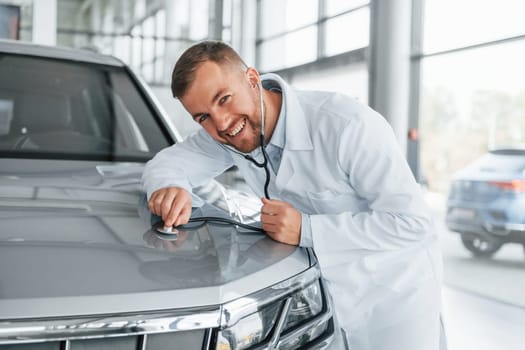 Medic in white coat is using stethoscope on the automobile.