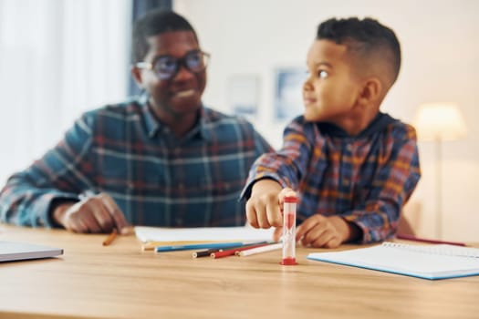 Sitting by the table with laptop. African american father with his young son at home.