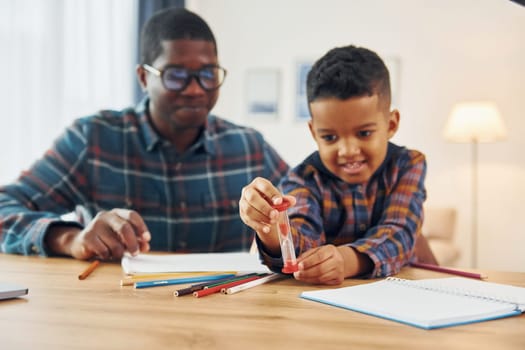 Sitting by the table with laptop. African american father with his young son at home.