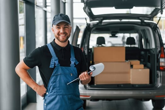 With document. Delivery man in uniform is indoors with car and with order.