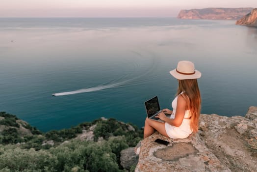 Freelance women sea working on the computer. Good looking middle aged woman typing on a laptop keyboard outdoors with a beautiful sea view. The concept of remote work