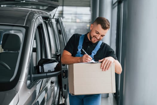 Paper box. Delivery man in uniform is indoors with car and with order.