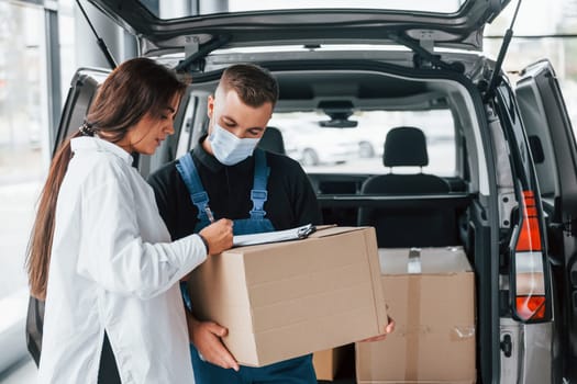 With woman. Delivery man in uniform is indoors with car and with order.