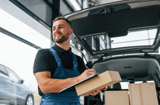 Portrait of delivery man in uniform that is indoors with car and with order.