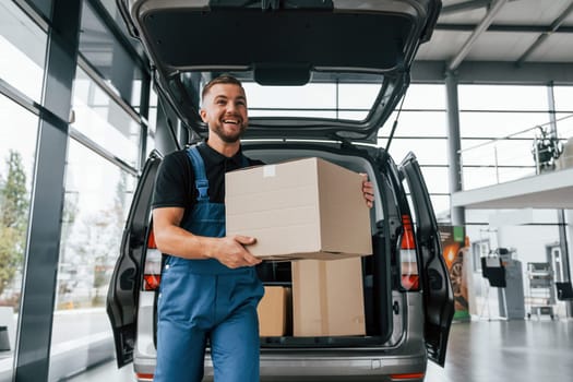 Front view. Delivery man in uniform is indoors with car and with order.