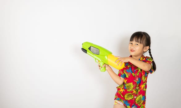 Happy Songkran Day, Asian kid girl with floral shirt hold water gun, Thai child funny hold toy water pistol and smile, isolated on white background, Thailand Songkran festival national culture concept