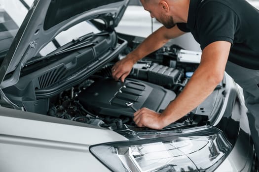 Some problems under the hood. Man in uniform is working in the autosalon at daytime.