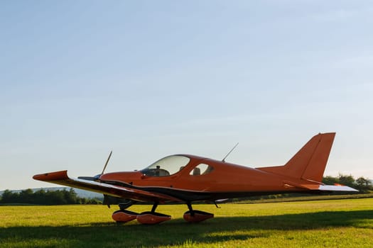 A small 2-seater plane against a blue sky with white clouds. Back view. Airplane on the field with grass.