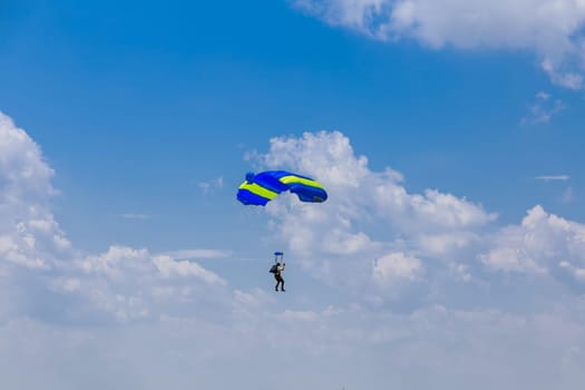 11 July 2021 Skutec, Czech Republic. Parachutist with yellow and blue parachute on blue sky background having fun flying from height to the ground, sports aerial entertainment. Air sports.