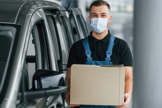 Business of service. Delivery man in uniform is indoors with car and with order.
