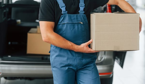 Business of service. Delivery man in uniform is indoors with car and with order.