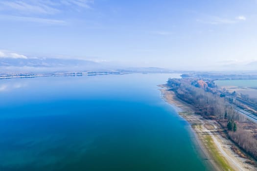 View from a height of the blue lake, road and beaches. Light morning fog over the lake. Panoramic view of the lake.