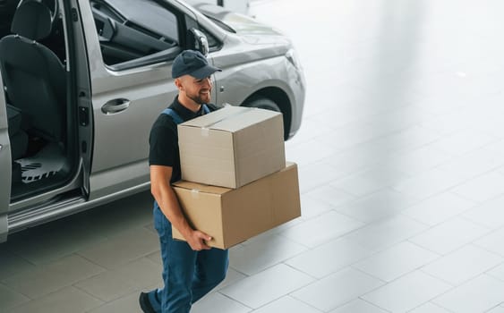 Business of service. Delivery man in uniform is indoors with car and with order.