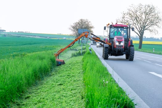 11 May 2022 Crudim, Czech Republic. A tractor with a rotary mower mows green grass near the road. Cleaning sidewalks, mowed roadsides.