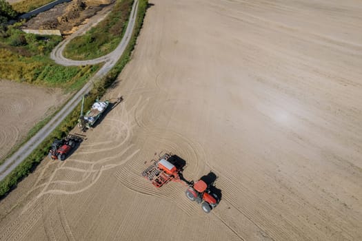 Grain seeder attached to a tractor sows grain in the field. Grain loader and trailer. Top view of modern equipment. Sowing grain.