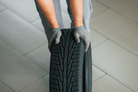 Installing new tire. Man in uniform is working in the autosalon at daytime.
