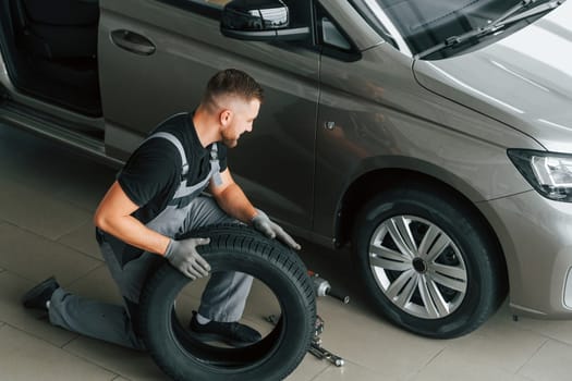 Installing new tire. Man in uniform is working in the autosalon at daytime.