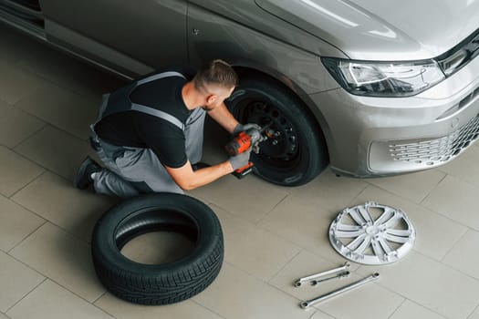 Installing new tire. Man in uniform is working in the autosalon at daytime.