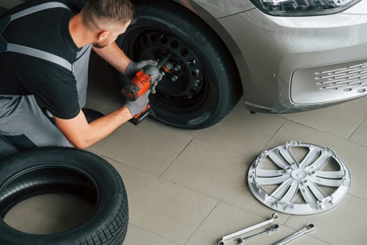 Installing new tire. Man in uniform is working in the autosalon at daytime.