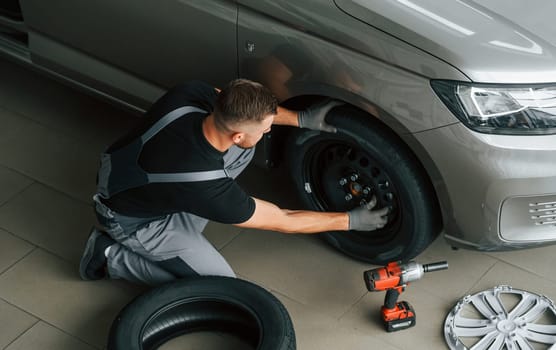 Installing new tire. Man in uniform is working in the autosalon at daytime.