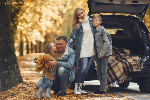 Near car with open trunk. Happy family is in the park at autumn time together.