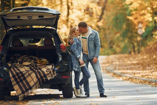 Opened trunk. Couple standing on the road in park near automobile.
