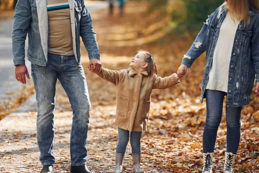 Holding daughter by hands. Happy family is in the park at autumn time together.