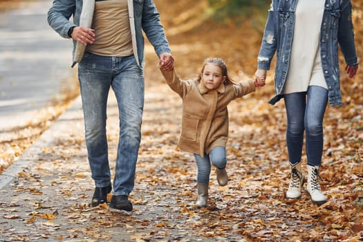Holding daughter by hands. Happy family is in the park at autumn time together.
