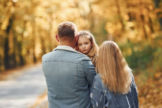 Little girl with her parents. Happy family is in the park at autumn time together.