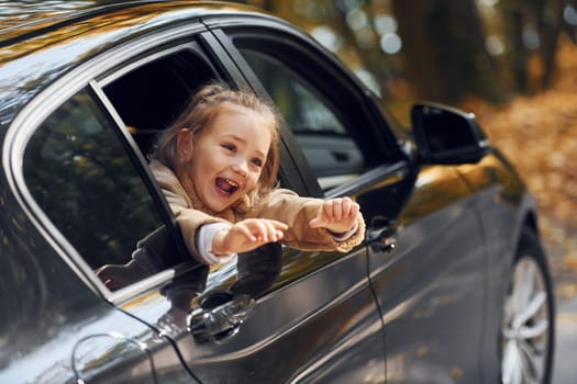 Little girl sitting in the black automobile and looking through the window.