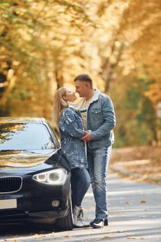 Couple standing on the road in park near automobile.