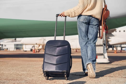 With lugagge. Young female passanger in casual clothes is outdoors near the plane.