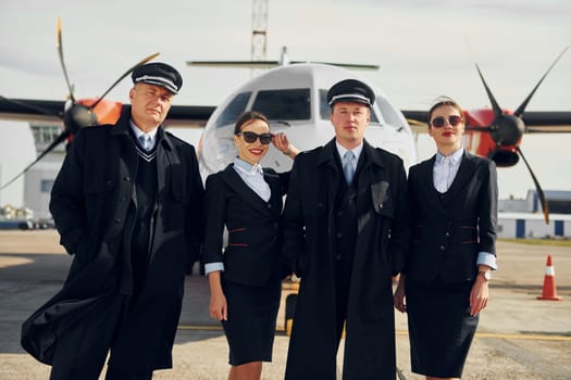Two men and two women. Crew of airport and plane workers in formal clothes standing outdoors together.