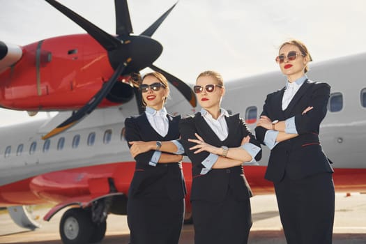 Three stewardesses. Crew of airport and plane workers in formal clothes standing outdoors together.