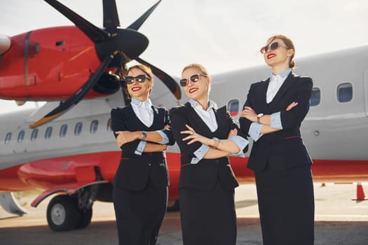 Three stewardesses. Crew of airport and plane workers in formal clothes standing outdoors together.
