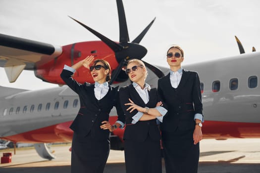 Three stewardesses. Crew of airport and plane workers in formal clothes standing outdoors together.