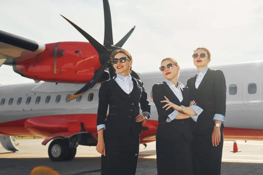 Three stewardesses. Crew of airport and plane workers in formal clothes standing outdoors together.