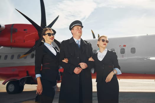 Three people. Crew of airport and plane workers in formal clothes standing outdoors together.