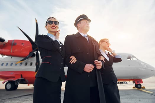 Three people. Crew of airport and plane workers in formal clothes standing outdoors together.