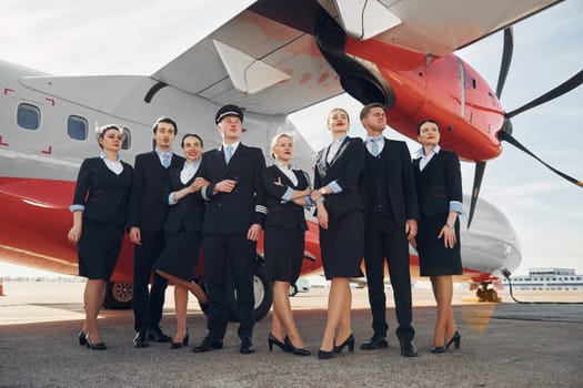 Near plane. Crew of airport workers in formal clothes standing outdoors together.