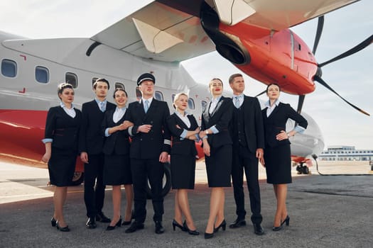 Near plane. Crew of airport workers in formal clothes standing outdoors together.