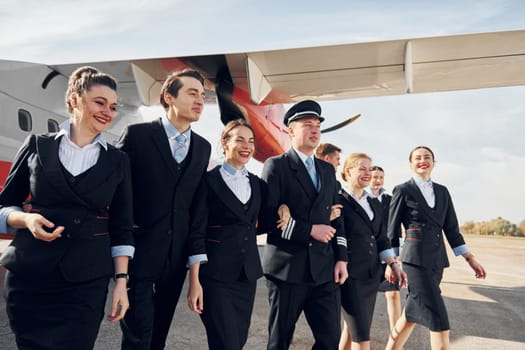 Crew of airport and plane workers in formal clothes standing outdoors together.