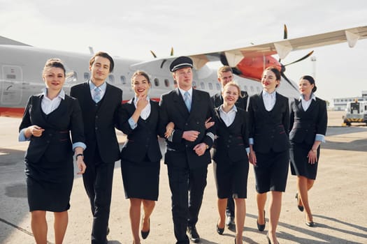 Crew of airport and plane workers in formal clothes standing outdoors together.