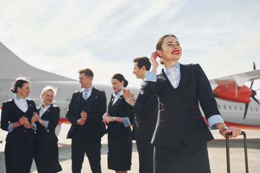 Crew of airport and plane workers in formal clothes standing outdoors together.