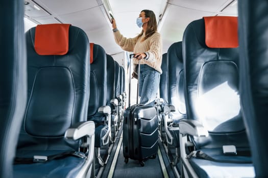 With lugagge. Young female passanger in casual clothes is in the plane.