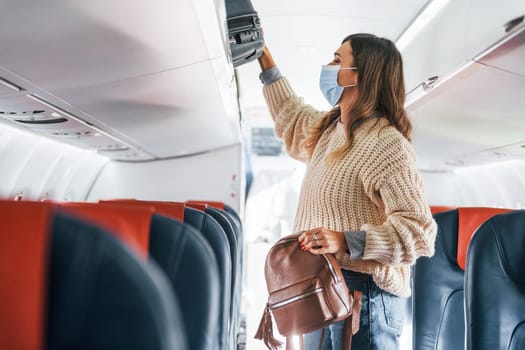 With lugagge. Young female passanger in casual clothes is in the plane.